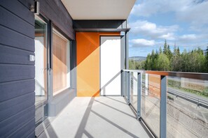 Ein Balkon mit Metallgeländer, ein Fenster mit Jalousien und Blick auf ein bewaldetes Gebiet.