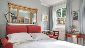Quarto com uma cama grande, uma escrivaninha, uma cadeira, uma janela com cortinas e um espelho com moldura decorativa.