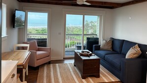 Una sala de estar con techo de madera, un sofá azul oscuro, sillones a rayas, una mesa de centro de madera y un televisor en la pared.