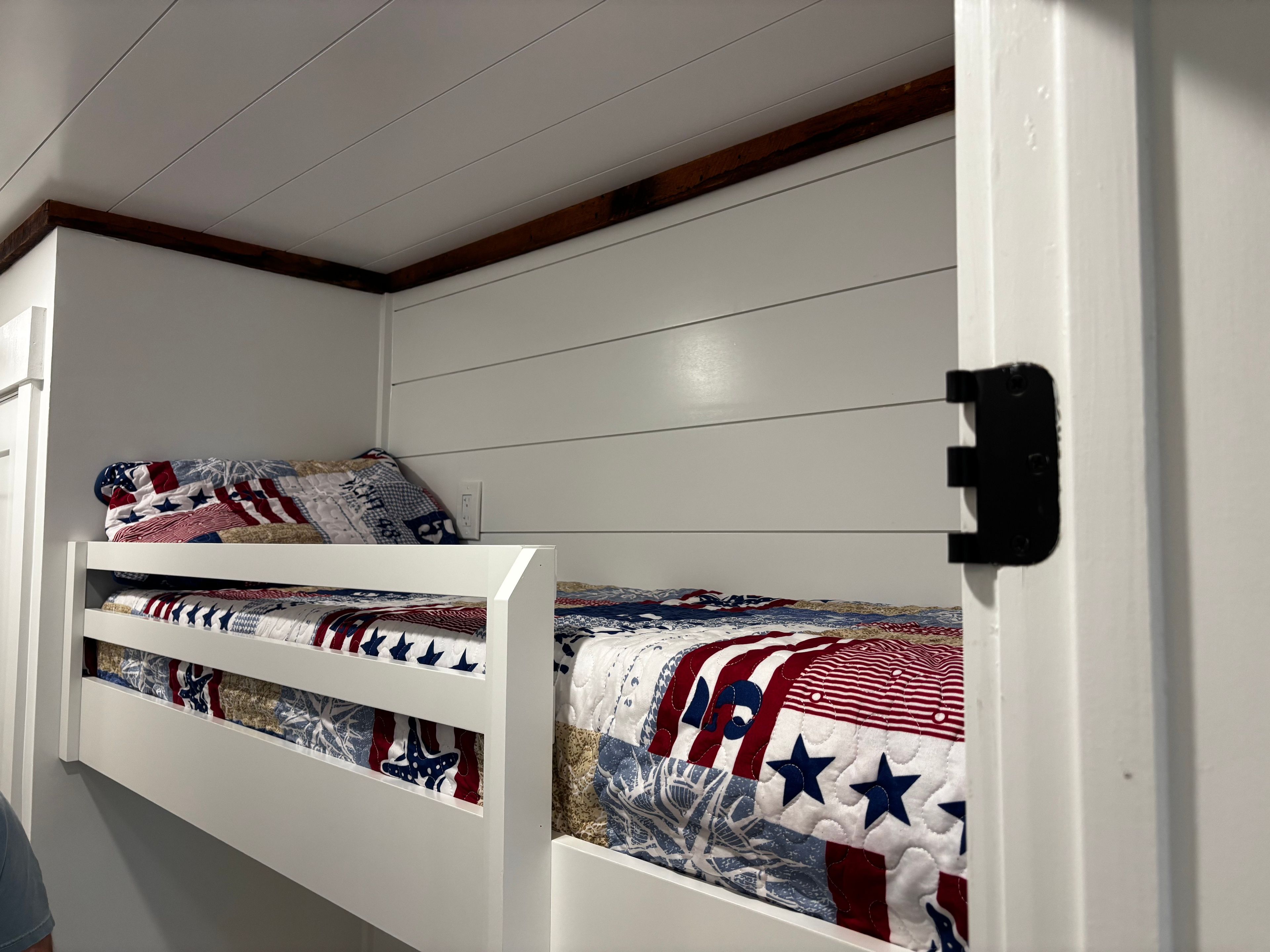 Una cama litera con cabecera y piecera acolchados, una pared blanca y un techo con vigas de madera.