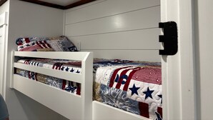 Una cama litera con cabecera y piecera acolchados, una pared blanca y un techo con vigas de madera.