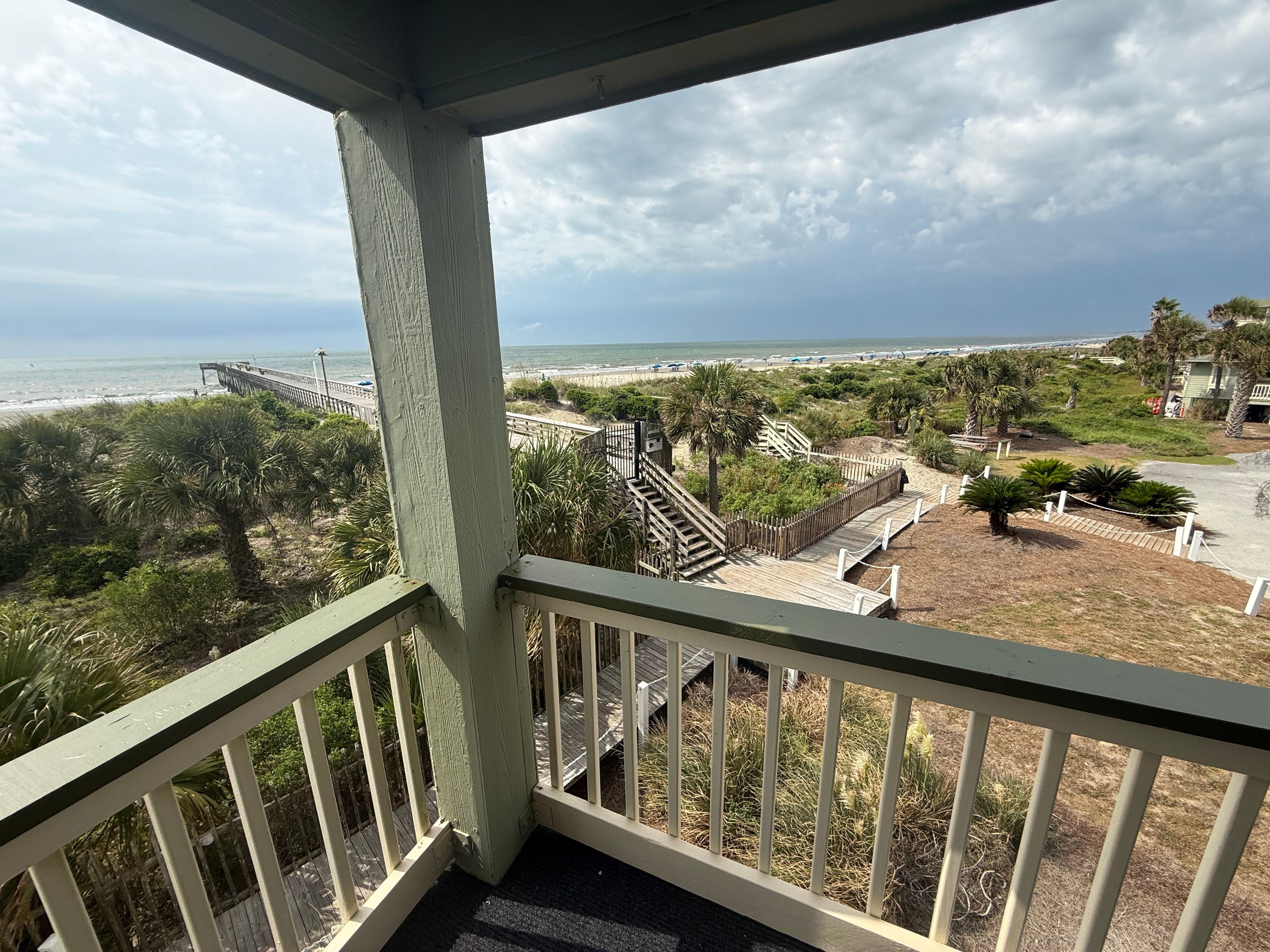 Un balcón con vista a una playa, una escalera de madera y una valla.