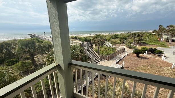 Un balcón con vista a una playa, una escalera de madera y una valla.
