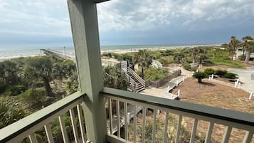 Un balcón con vista a una playa, una escalera de madera y una valla.