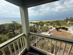 Un balcon donnant sur une plage, un escalier en bois et une clôture.