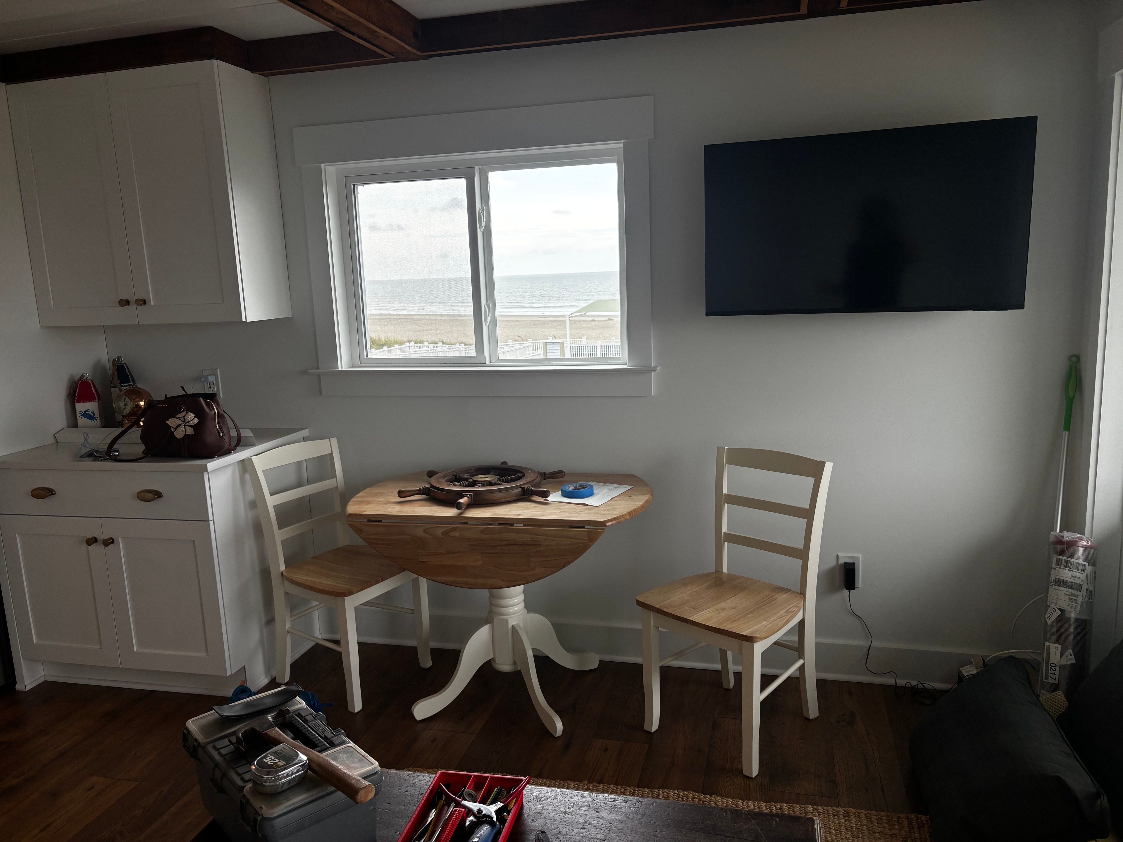 Une pièce avec une table en bois, deux chaises, un téléviseur et une fenêtre donnant sur la plage.