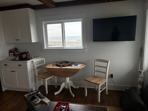 Une pièce avec une table en bois, deux chaises, un téléviseur et une fenêtre donnant sur la plage.