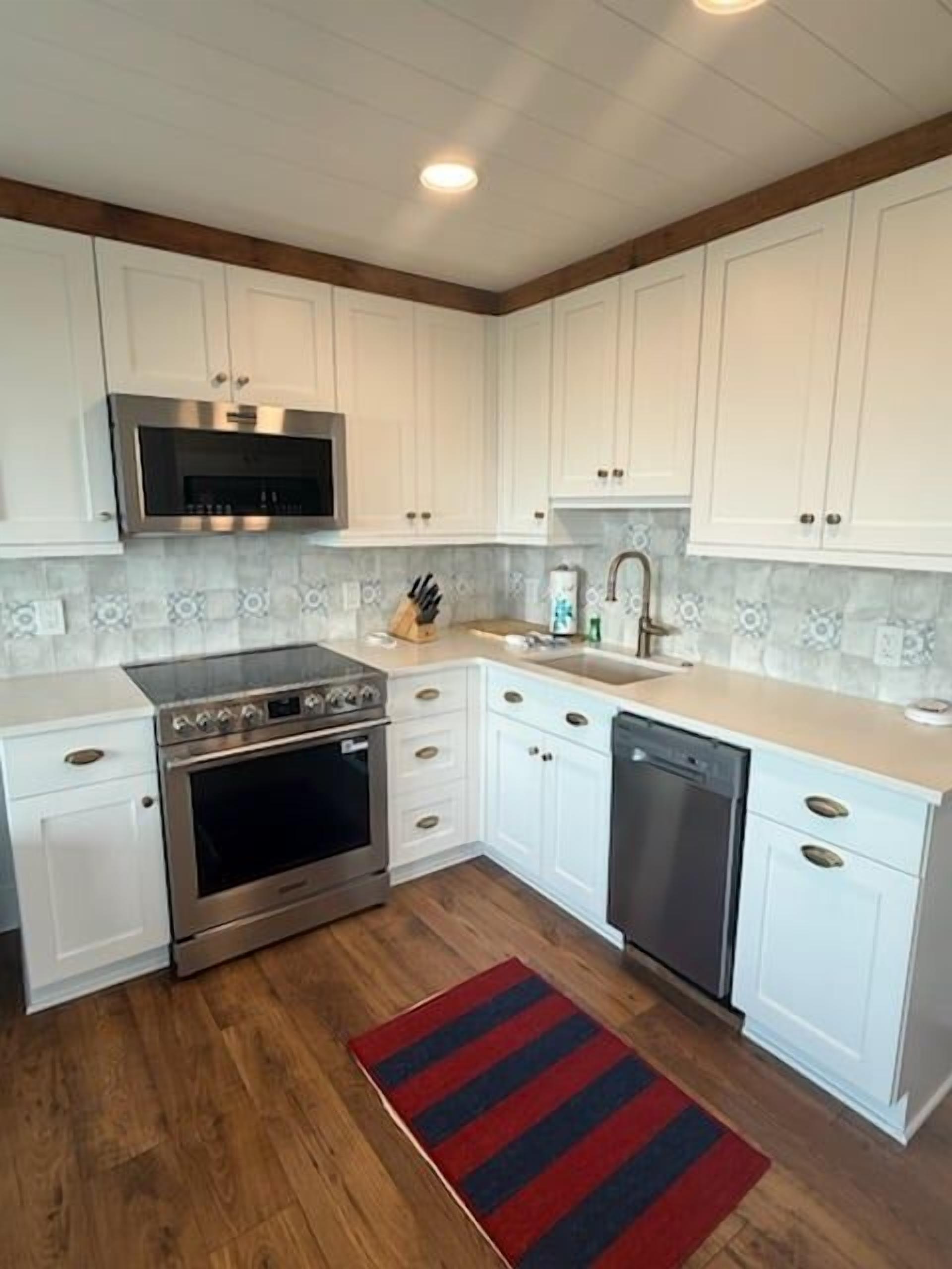 A kitchen with white cabinets, a stainless steel range, a dishwasher, and a red striped rug.