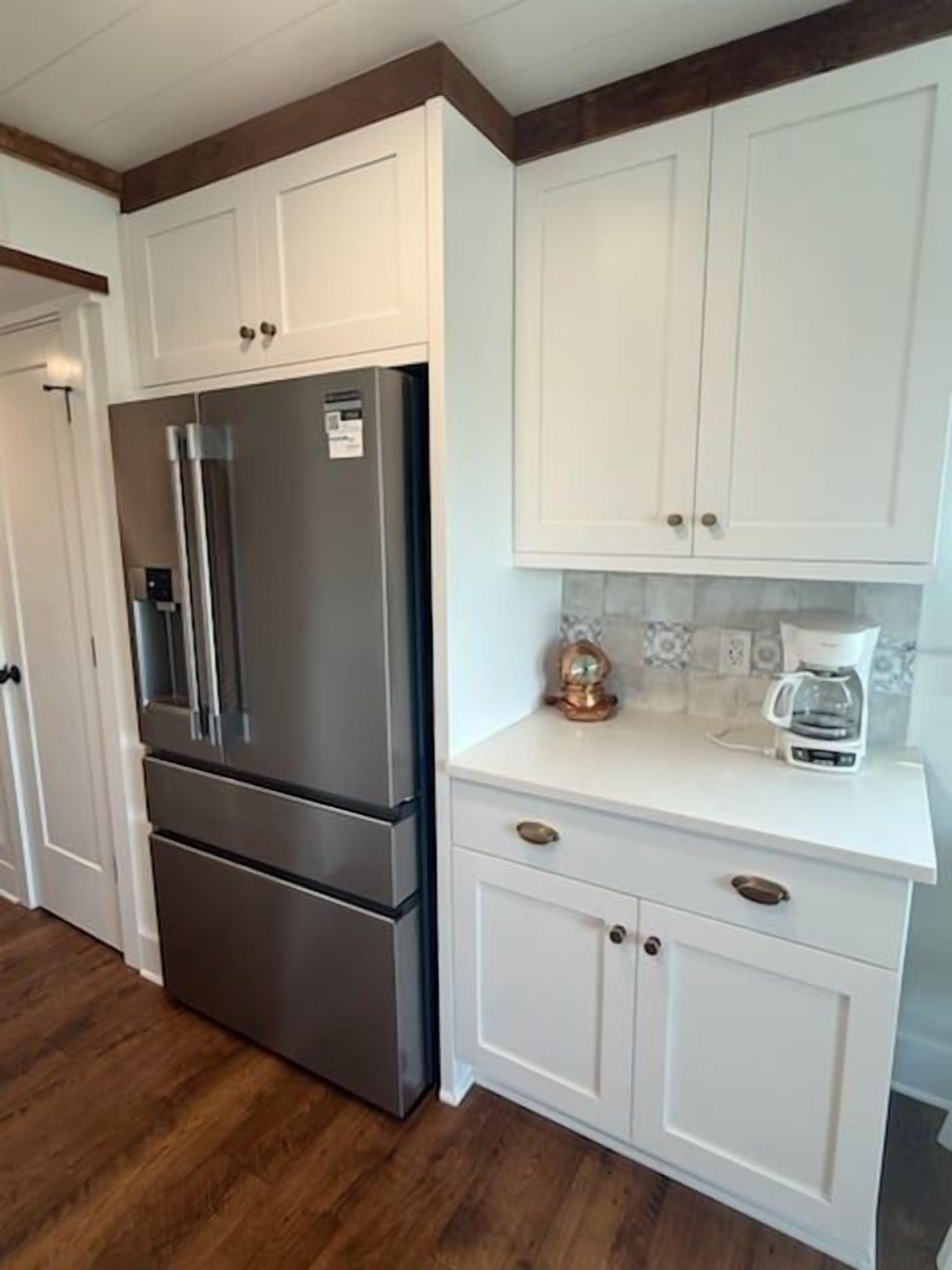 A kitchen with white cabinets, a stainless steel refrigerator, and a coffee maker on the countertop.