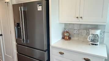 A kitchen with white cabinets, a stainless steel refrigerator, and a coffee maker on the countertop.