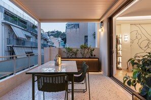 A balcony with a table and chairs, a view of the cityscape, and a bookshelf with decorative items. - Acropolis Luxury Penthouse with Private Jacuzzi, Apartment (Athens)