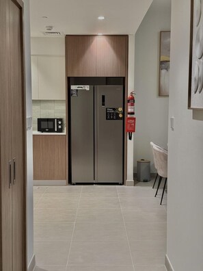 A modern kitchen with a built-in stainless steel refrigerator, a microwave, and a small trash bin.