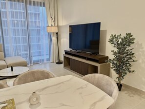 Ein modernes Wohnzimmer mit Fernseher, einer Couch, einem Esstisch und einer Topfpflanze.