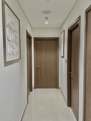 A hallway with a wooden door at the end, a light switch on the wall, and a ceiling light fixture.