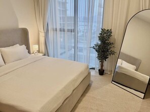 Ein Hotelzimmer mit einem großen Bett, einem Nachttisch mit Lampe, einer Topfpflanze und einem Spiegel.