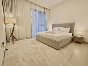 A bedroom with a bed, a bedside table, a lamp, and a window with curtains.