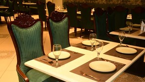 Un comedor con mesas dispuestas para dos, cada una con mantel individual, platos, cubiertos y copas de vino.