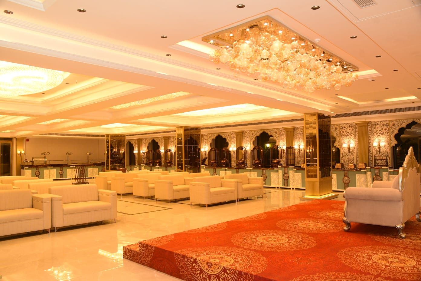 Un vestíbulo amplio con alfombra roja, sofás blancos y un candelabro.