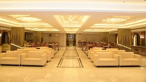 Een ruime hotellobby met een open centrale ruimte, zitgedeeltes en een weelderige kroonluchter.
