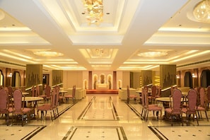 A spacious hotel lobby with a central seating area, multiple tables, and chairs arranged for guests.