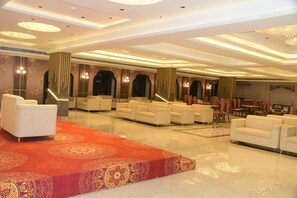 A spacious hotel lobby with a red carpet, multiple seating areas, and a grand staircase.