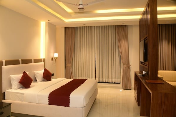 A hotel room with a large bed, a desk, a television, and curtains.