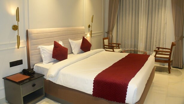 Habitación de hotel con una cama grande, dos mesitas de noche, una silla y una ventana con cortinas.