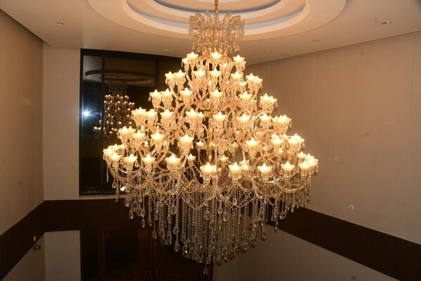 A large, ornate chandelier with multiple tiers and crystal decorations, suspended in a well-lit room with a reflective floor and a curved ceiling.