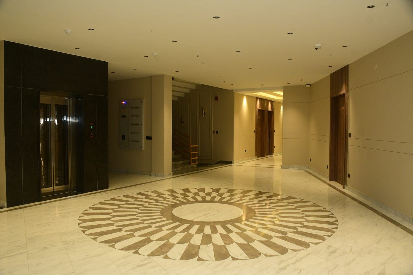 A hotel corridor with a central circular floor design, elevators, and doors.