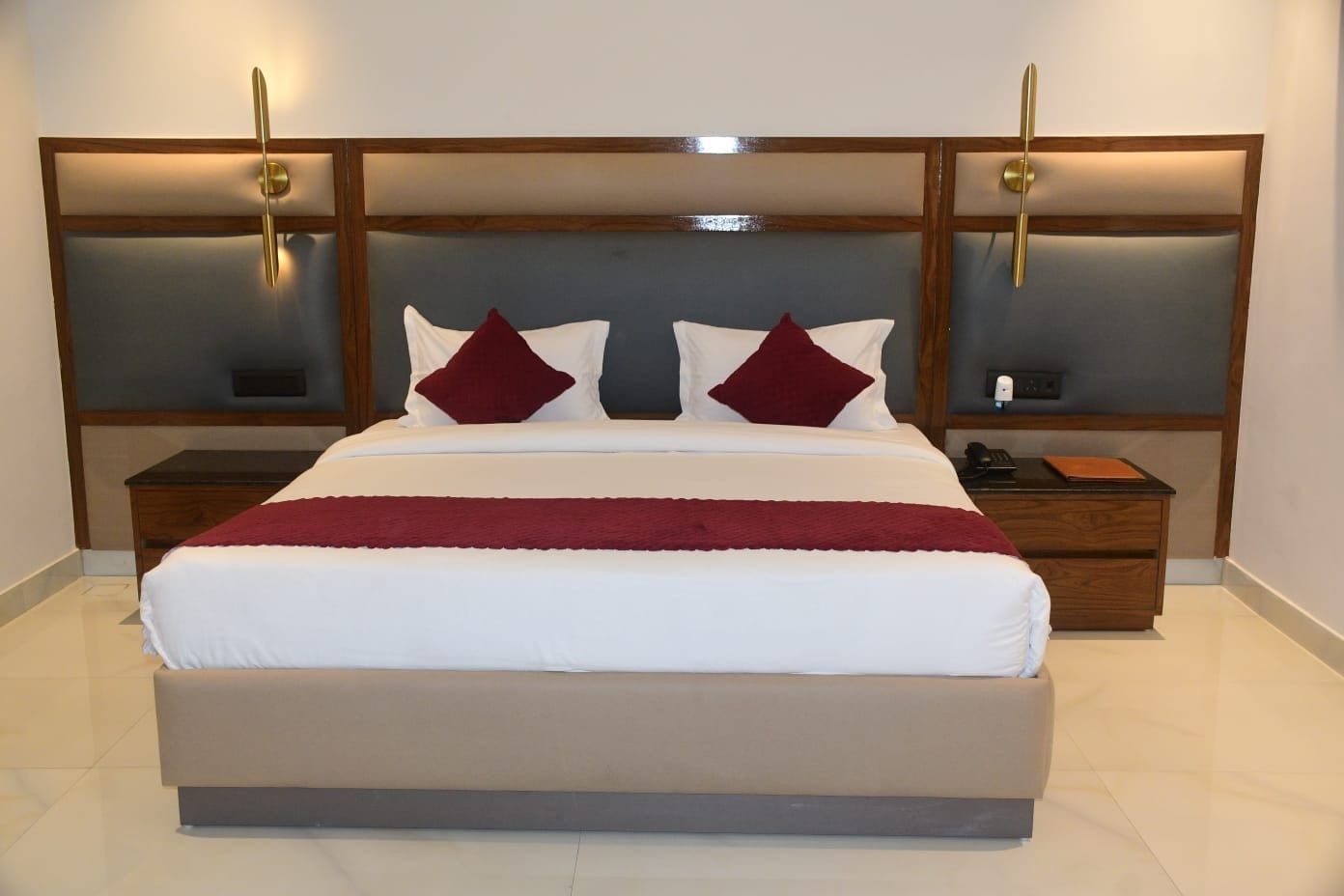 Una cama grande con cabecera de madera, dos mesitas de noche y una manta roja.