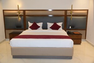 Una cama grande con cabecera de madera, dos mesitas de noche y una manta roja.