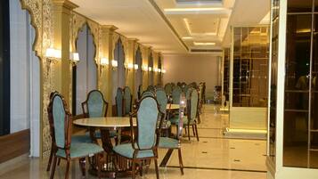 A hotel dining area with round tables and chairs, ornate wall decorations, and a modern ceiling design.