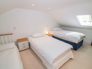 A bedroom with two single beds, a nightstand with a lamp, and a sloped ceiling. - Wayside (Moreton-in-Marsh)