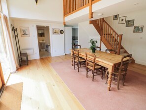A dining area with a wooden table and chairs, a staircase, and a view of the kitchen. - Wayside (Moreton-in-Marsh)