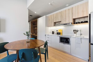 A modern kitchen with a wooden dining table, chairs, and built-in appliances. - The Acre by Neighbourgood (Cape Town)