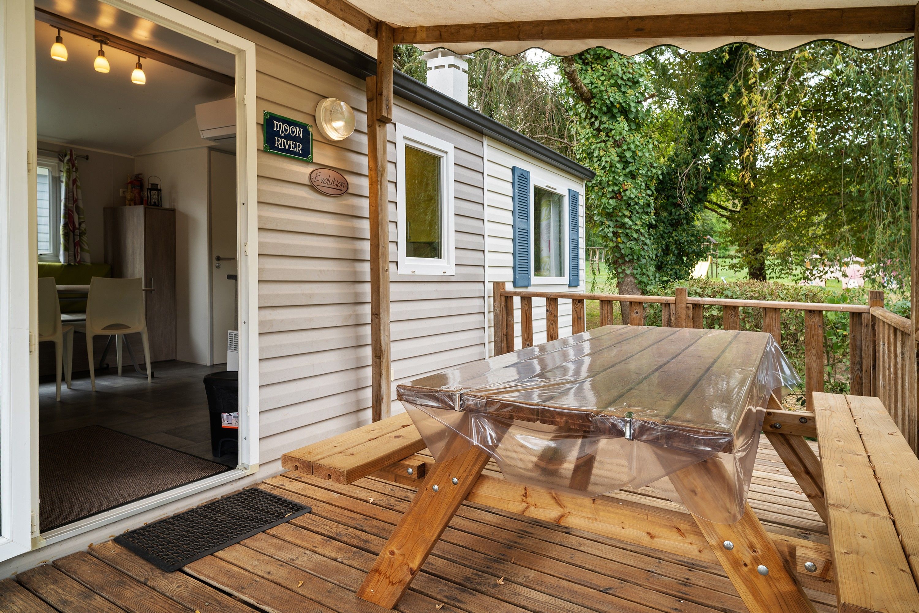 Une terrasse en bois avec un matelas, une porte donnant sur une pièce et une pancarte sur laquelle on peut lire : « Moon River Evolution ».