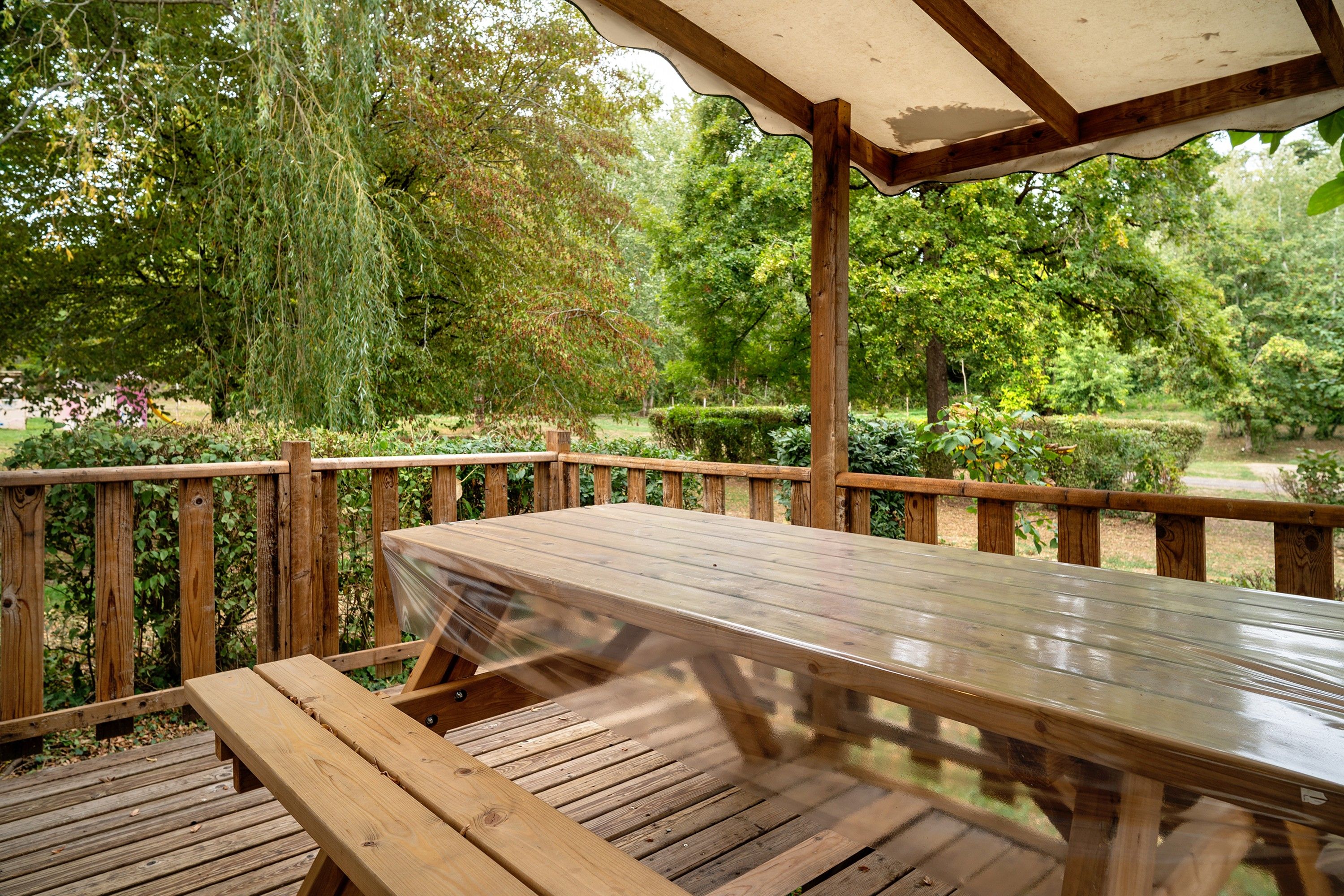 A wooden deck with a table and benches, surrounded by lush greenery and trees.