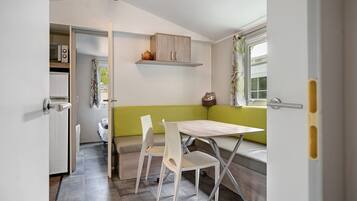 Une cuisine compacte avec un coin repas comprenant une table et des chaises, un banc et une fenêtre avec des rideaux.