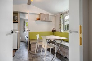 A compact kitchen with a dining area, including a table and chairs, a bench, and a window with curtains.