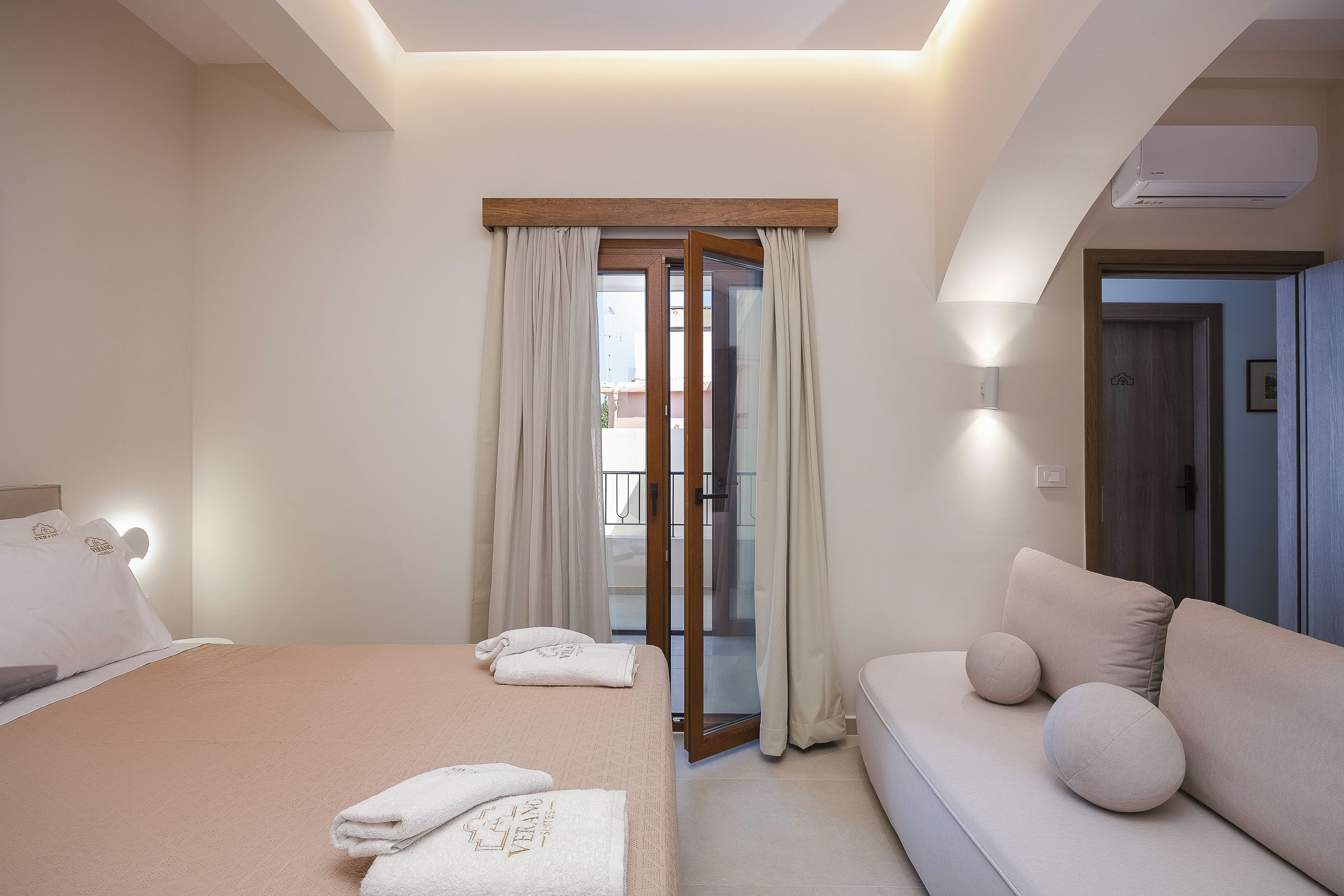 A hotel room with a bed, a sofa, a sliding glass door, and a ceiling light.