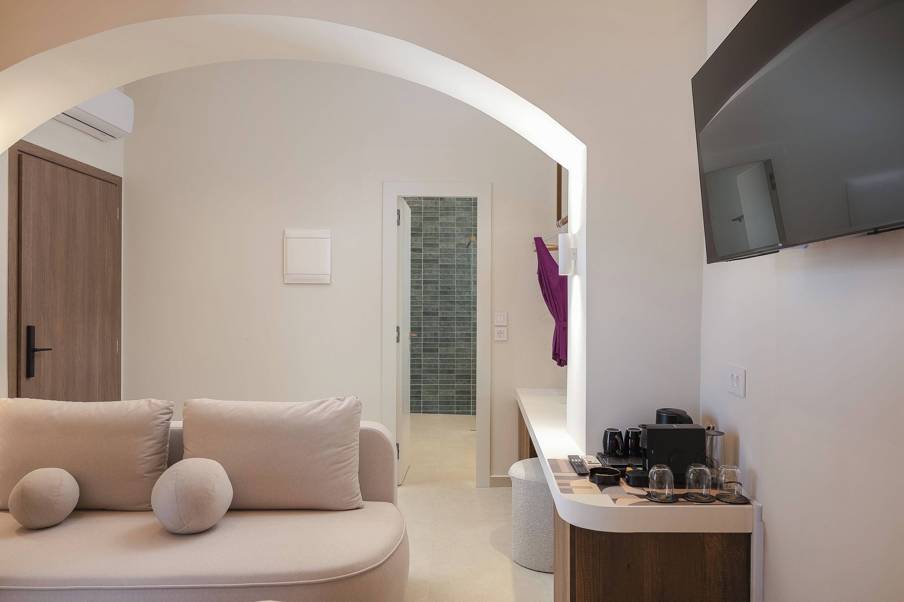 Ein modernes Hotelzimmer mit einer Couch, einer kleinen Küchenzeile, einem Fernseher und einem Badezimmer mit Dusche.
