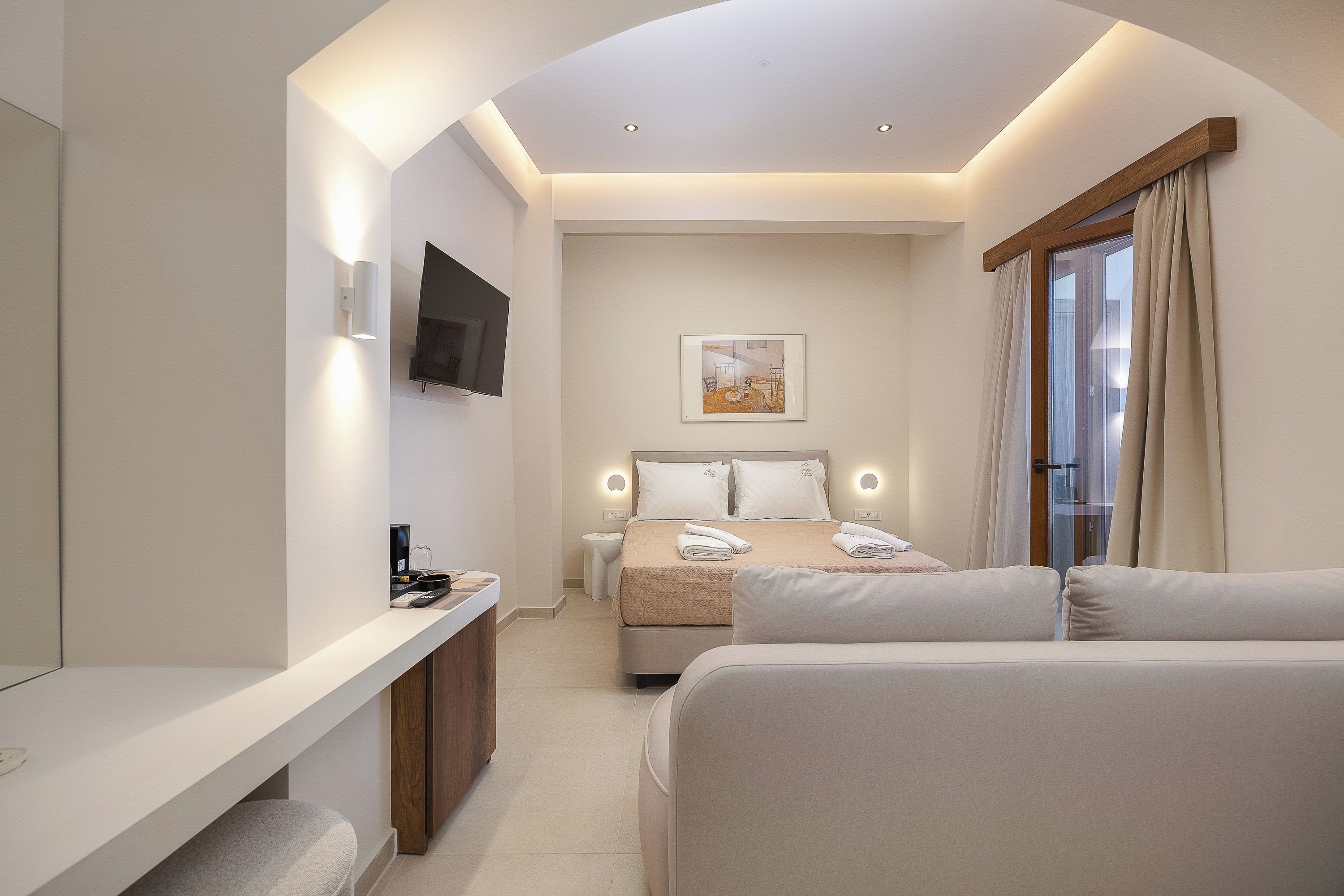 A modern hotel room with a bed, a bedside table, a TV mounted on the wall, and a window with curtains.