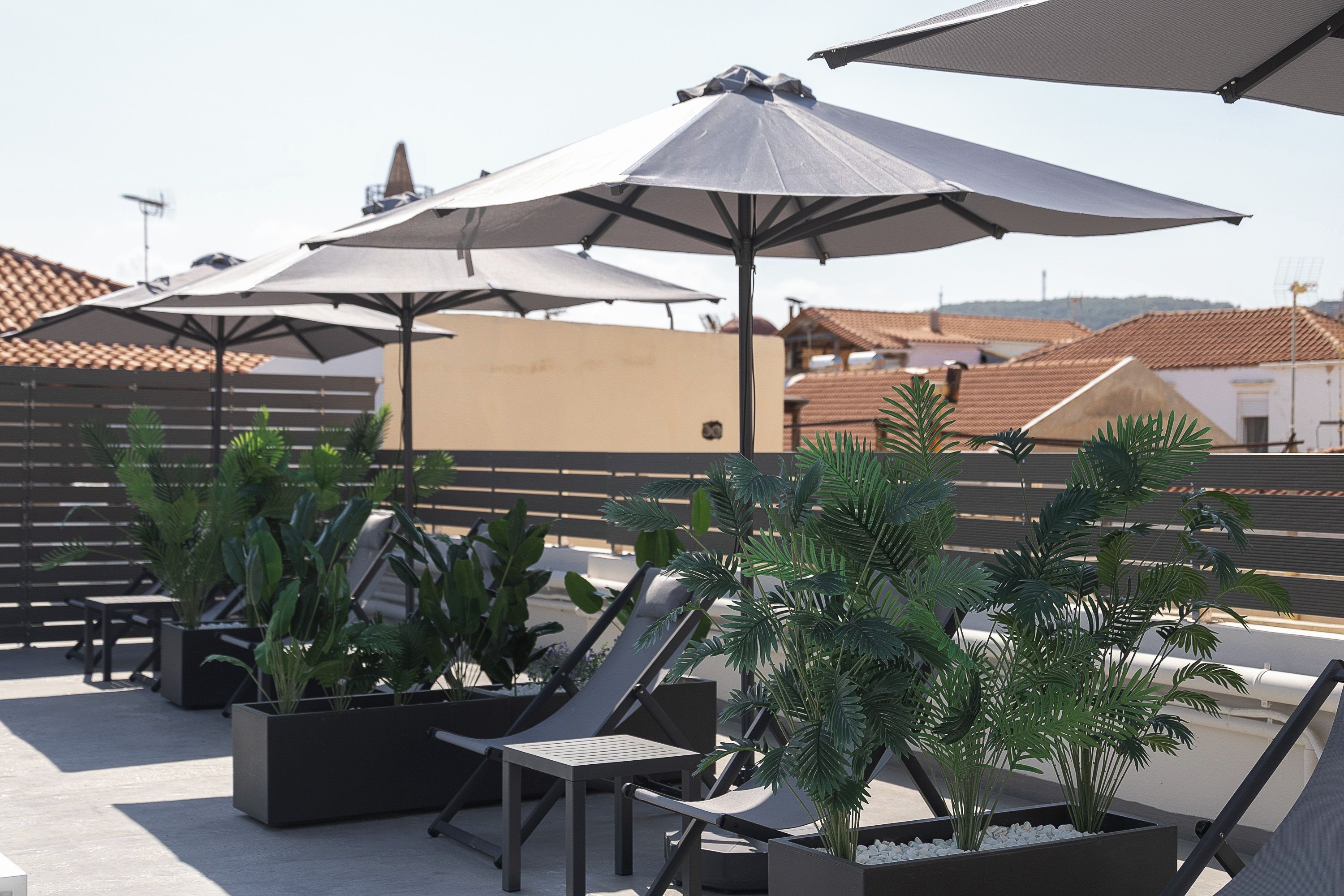Eine Dachterrasse mit mehreren Liegestühlen und Sonnenschirmen, umgeben von Topfpflanzen.