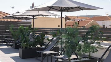 Eine Dachterrasse mit mehreren Liegestühlen und Sonnenschirmen, umgeben von Topfpflanzen.