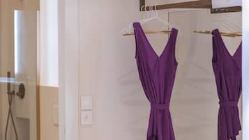 Ein Zimmer mit einer weißen Wand, einem hängbaren Kleiderständer mit violetten Kleidungsstücken und einer weißen Steckdose.