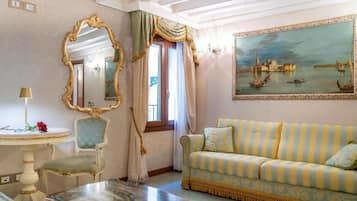 Una habitació amb un sofà estriat, una taula rodona, una cadira, un mirall i un quadre d'un paisatge urbà.