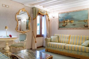 A room with a striped sofa, a round table, a chair, a mirror, and a painting of a cityscape. - Casa Guggenheim (Venezia)