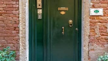 Una porta doble verda amb una nansa de bronze, un picapedra de bronze i una placa de bronze petita sobre la porta. Hi ha una finestra amb una reixa de metall per sobre de la porta, i dos fanals de paret a banda i banda.