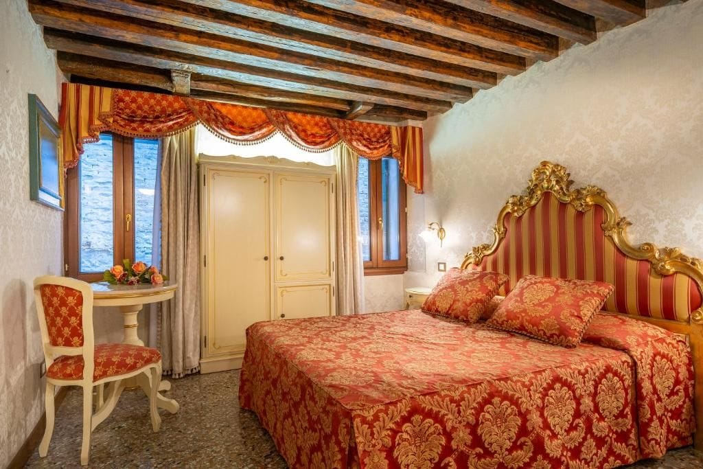 A bedroom with a bed, a chair, a table with flowers, and a window with curtains.