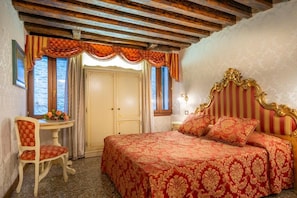 Un dormitorio con cama, una silla, una mesa con flores y una ventana con cortinas.